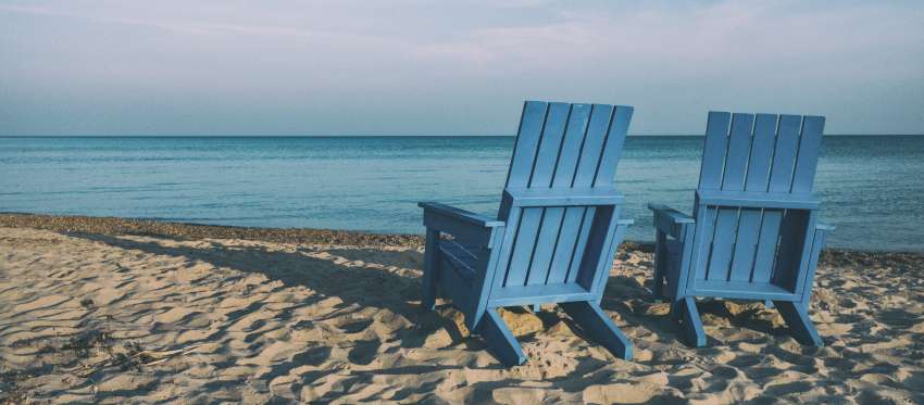 Two blue chairs on a beach facing the ocean.