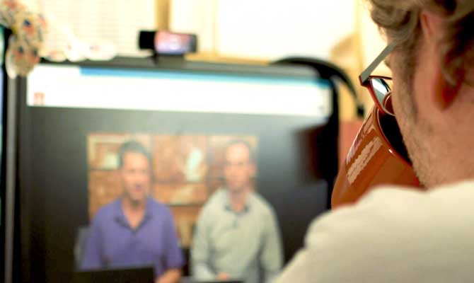 Close up of a video education course on a computer monitor with a student watching it and drinking a cup of coffee