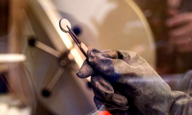 In a lab, a close up of a hands with an industrial pincer, holding a battery