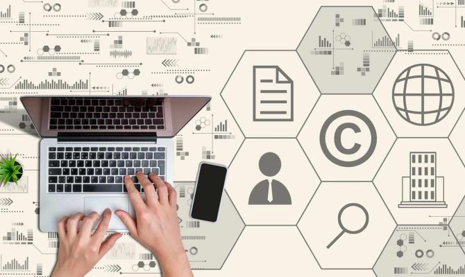 Top down view of hands on a laptop, with super-imposed icons representing copyrights and patents all around on the table