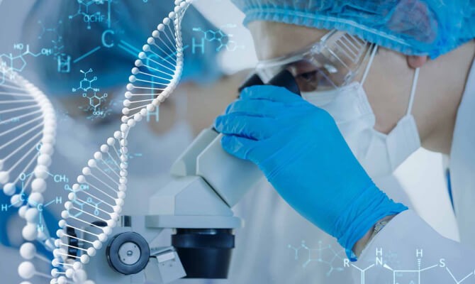 A person in medical protective equipment looks into a microscope.