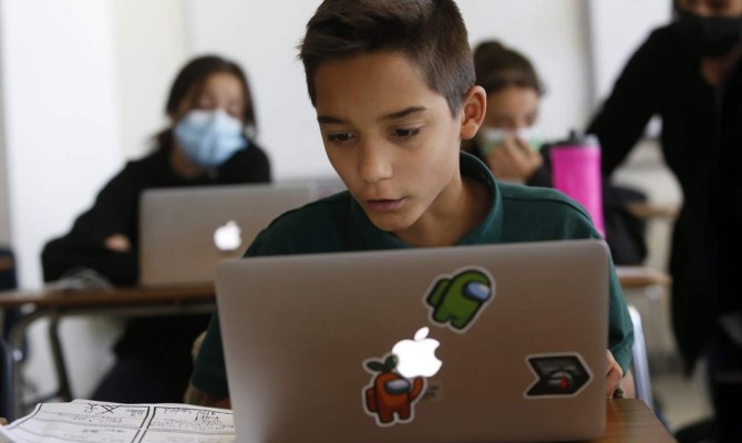 Grade school student learning coding in a class setting, looking at his laptop