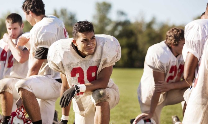 Football players kneeling at playing field on sunny day