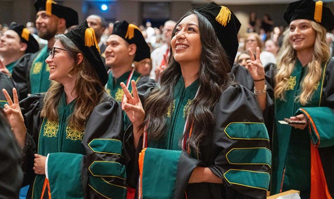 Medical graduates in green-trimmed academic regalia celebrate during a commencement ceremony at the UTRGV Performing Arts Complex.