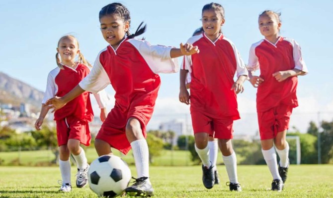 Young group of kids in red jerseys playing soccer
