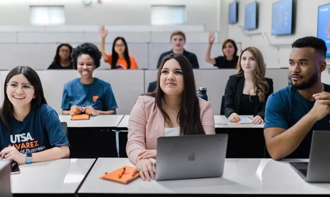 UT San Antonio students collaborate in a bright classroom, using laptops and taking notes.