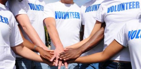 close up of people in a white shirts with the word "volunteer" on the front, with their hands in a center ready for breaking for teamwork