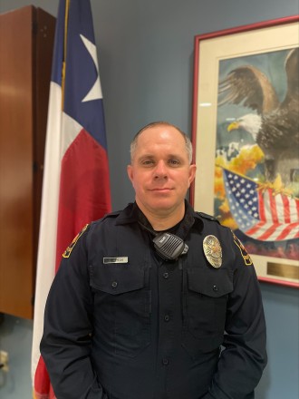 Officer Charles Speck stands in uniform in front of a State of Texas flag.