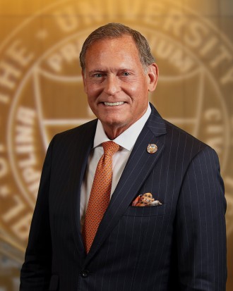 John M. Zerwas, MD, stands in front of a UT System Seal.