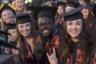 Male and female students smiling and wearing caps and gowns at graduation